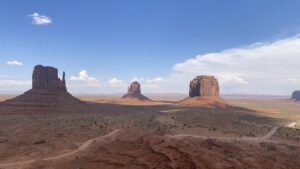 Formações rochosas icônicas no deserto de Monument Valley, sob um céu azul com nuvens esparsas, entre Utah e Arizona, nos Estados Unidos.