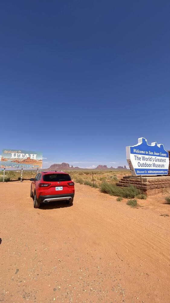 Carro parado em estrada de terra em frente à placa 'Welcome to Utah'
